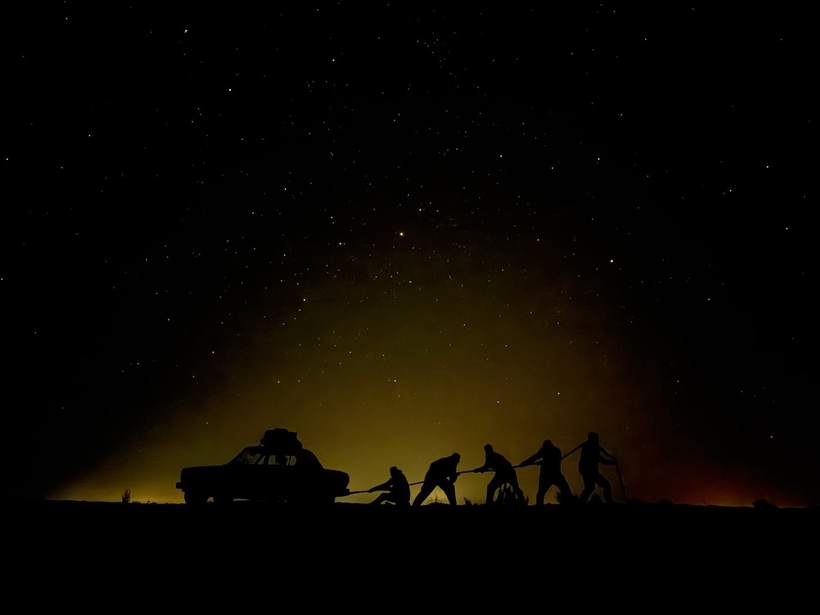 Siluety posádky ťahajúcej žigulu pod hviezdnou oblohou